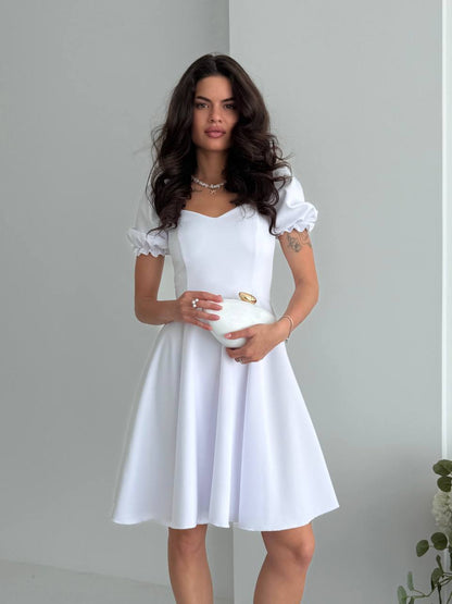 Woman wearing a white dress holding a clutch against a plain background