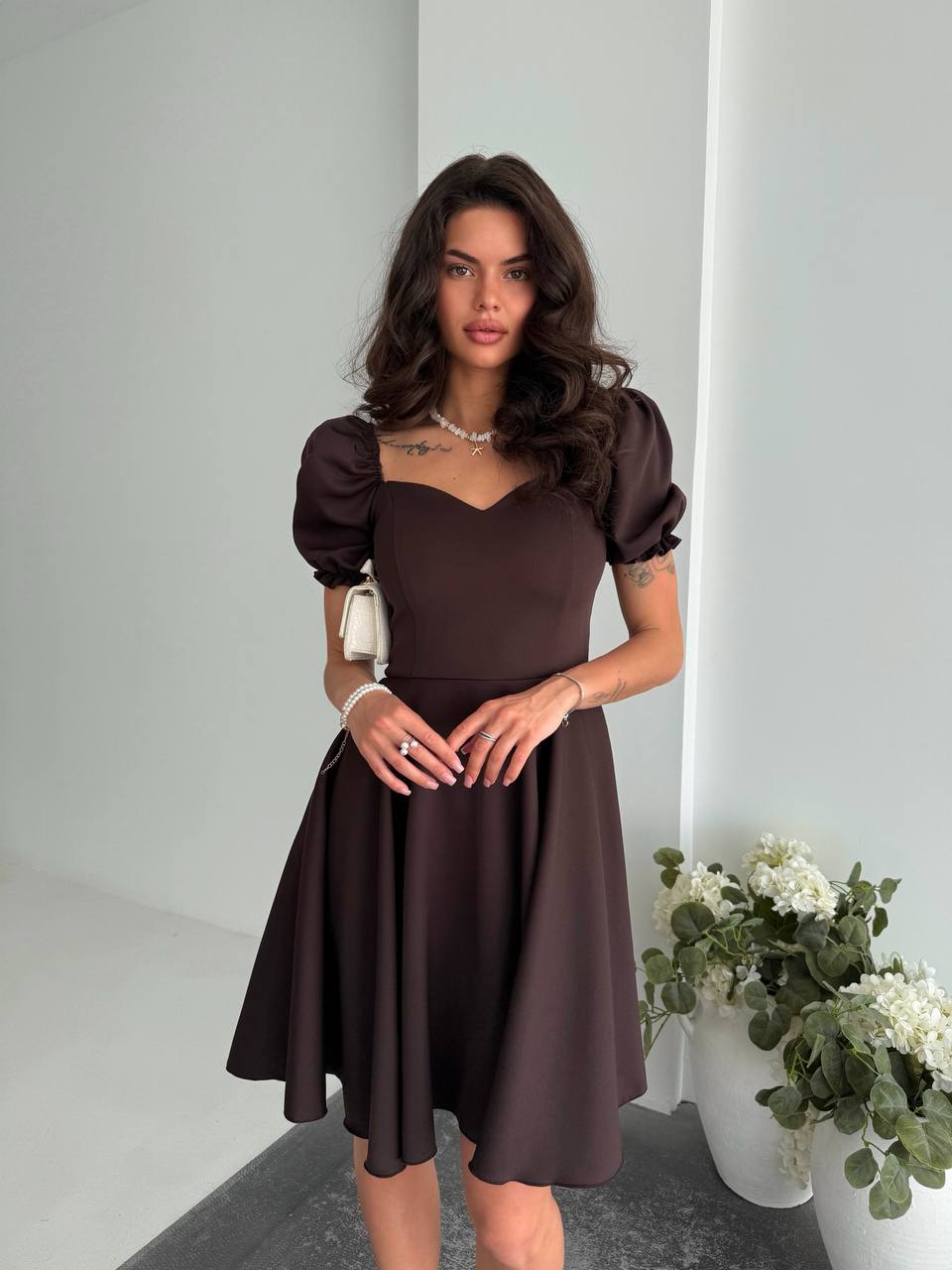 Woman wearing a brown dress with puffed sleeves in a minimalistic setting.