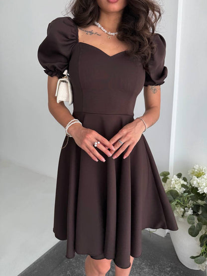 Woman wearing a brown dress with puffed sleeves in an indoor setting.