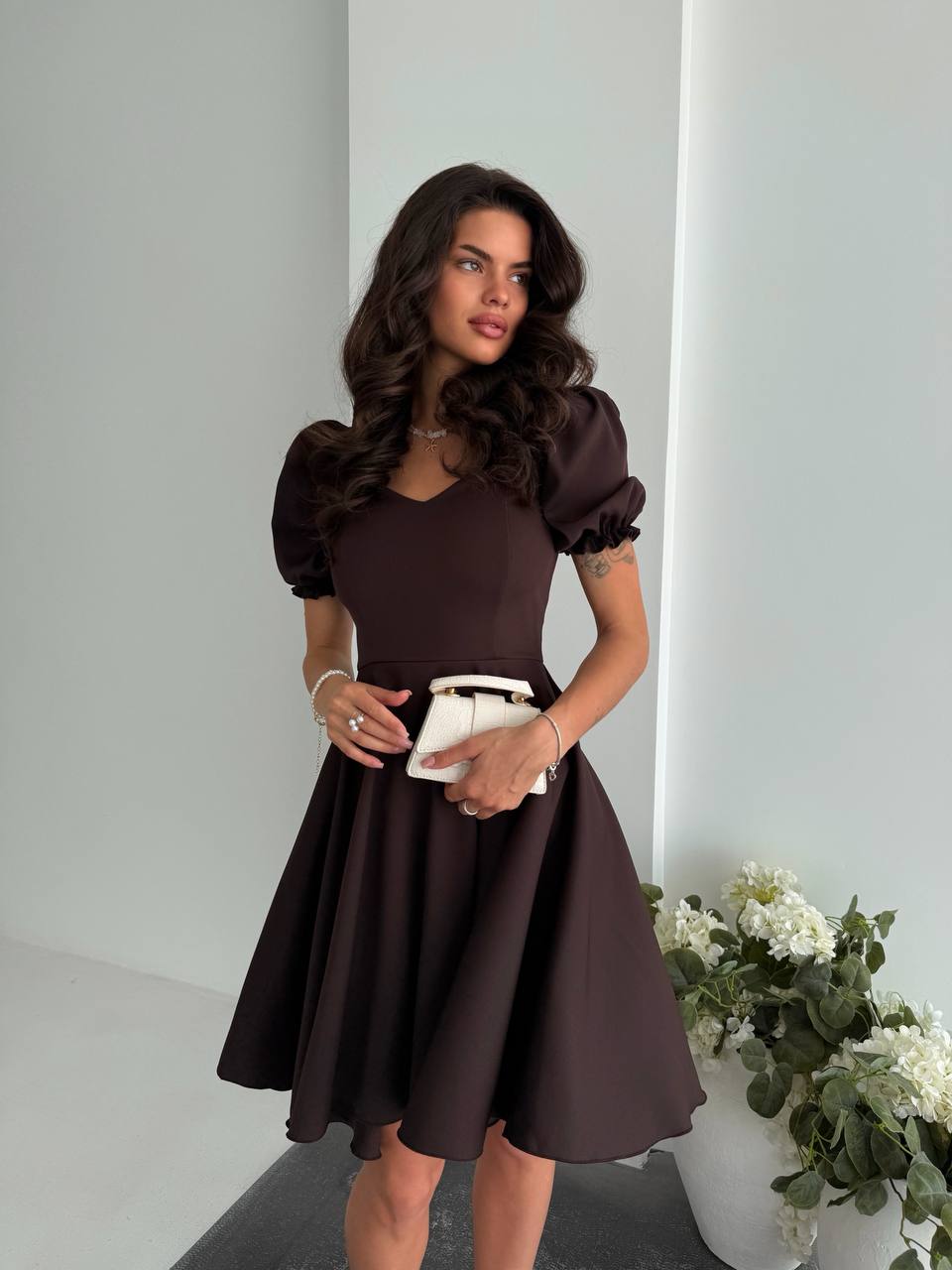 Woman wearing a brown dress with puffed sleeves in a minimalistic setting.