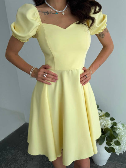 Woman wearing a yellow dress with puffed sleeves against a neutral background