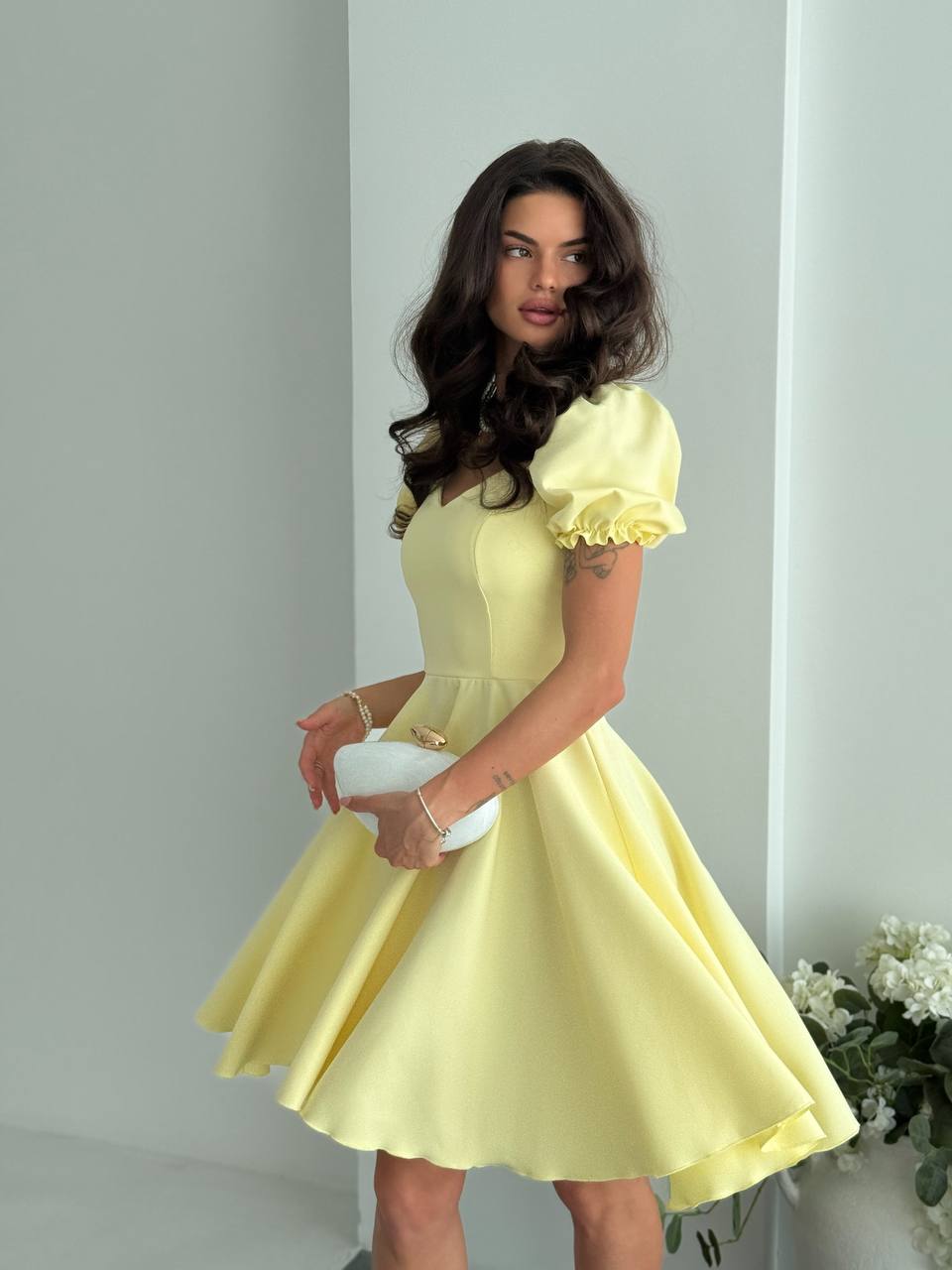 Woman wearing a yellow dress holding a white clutch against a light gray background