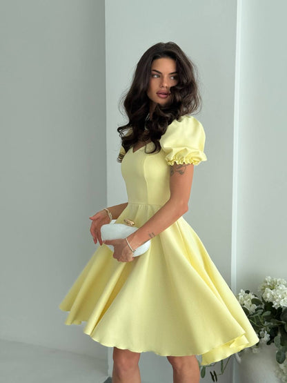 Woman wearing a yellow dress holding a white clutch against a light gray background