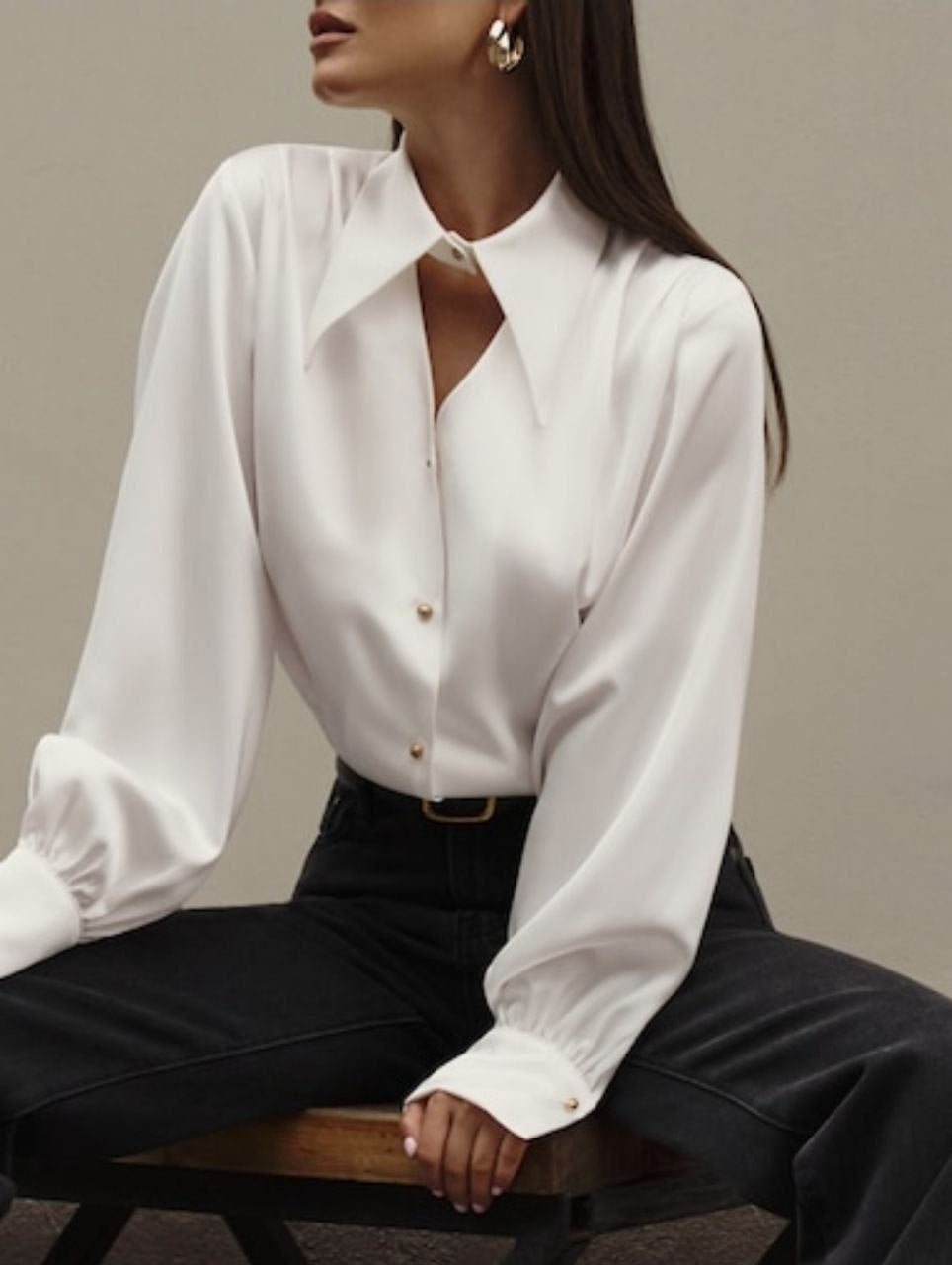 Person wearing a white blouse with long sleeves and black pants on a neutral background