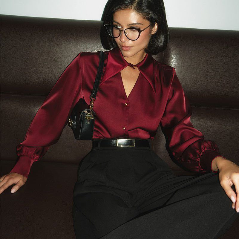 Woman wearing a red satin blouse and black pants sitting on a brown couch.