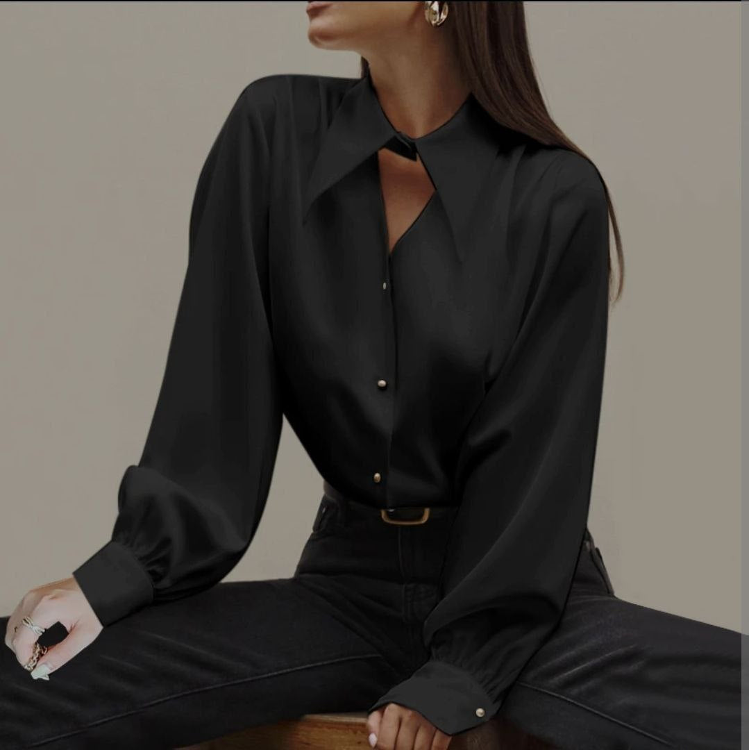 Person wearing a black blouse and pants sitting on a wooden stool against a neutral background