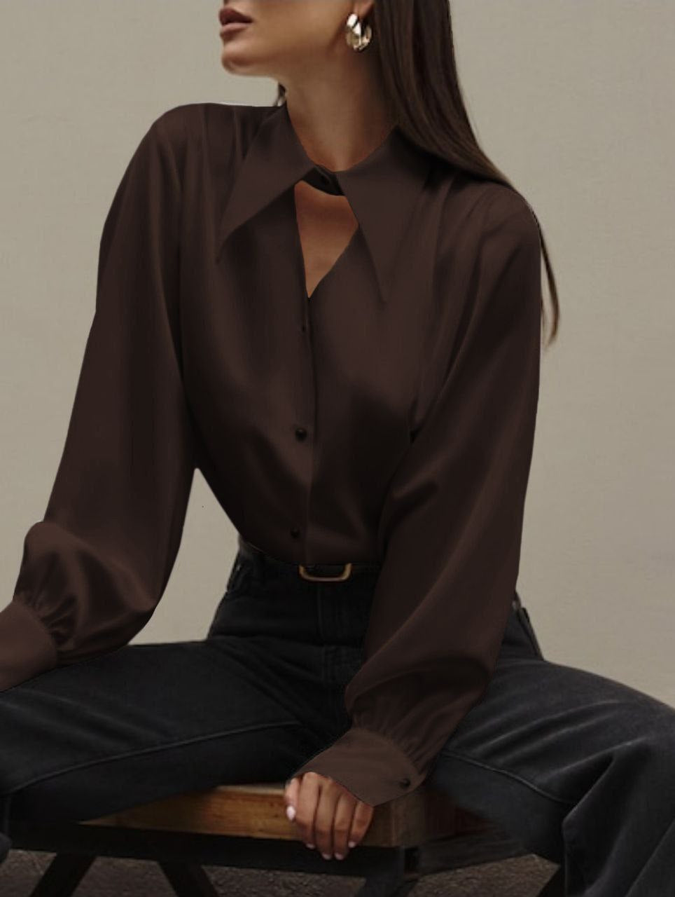 Woman wearing a dark brown blouse and black pants sitting on a wooden stool against a neutral background