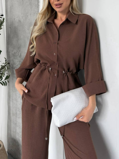 Woman wearing a brown outfit holding a white clutch against a neutral background