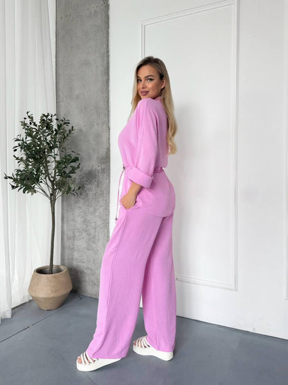 Woman in a pink outfit standing in a room with a plant and white door.