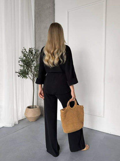 Person in black outfit holding a woven bag in a minimalistic room.