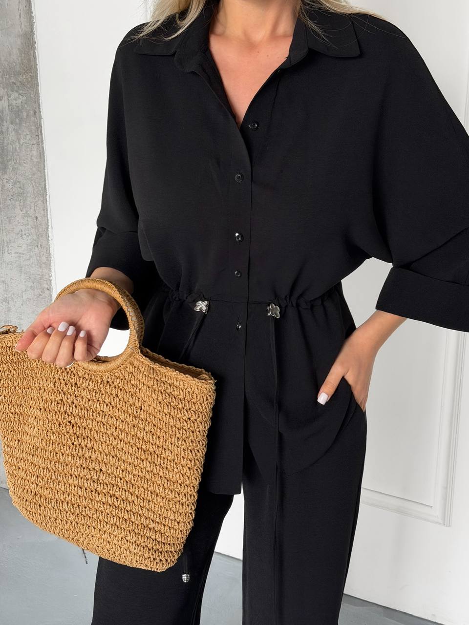 Person wearing a black outfit holding a woven beige handbag.
