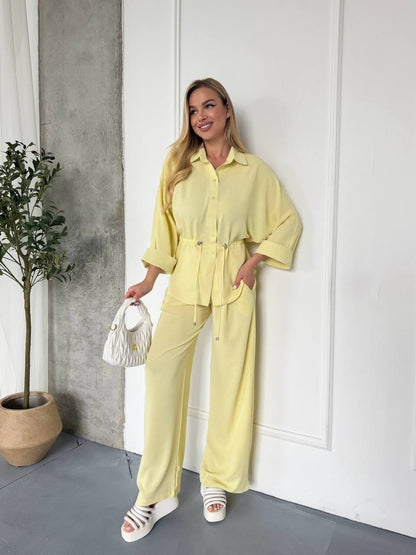 Woman in a yellow outfit standing indoors with a plant and white wall in the background