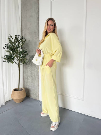 Woman in a yellow outfit standing in a room with a plant and white walls.