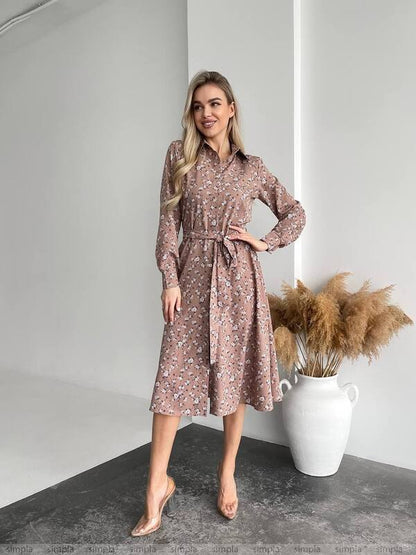 Woman wearing a floral dress standing in a minimalistic room with a vase of dried plants.