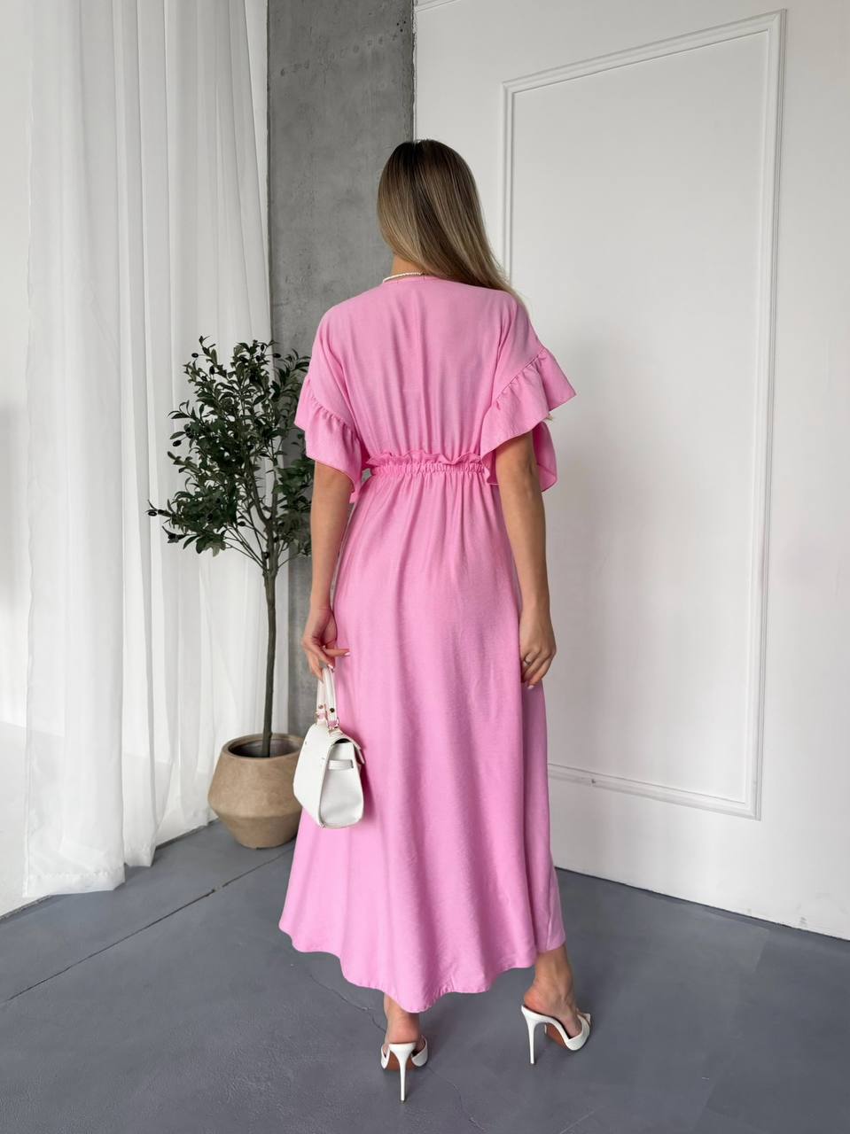 Woman wearing a pink dress in a minimalistic room with white walls and a plant.