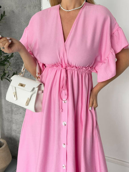 Woman wearing a pink dress holding a white handbag against a neutral background