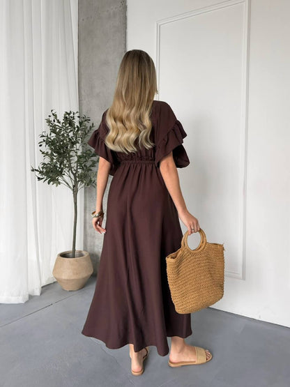 Woman in a brown dress holding a woven bag in a minimalistic room.