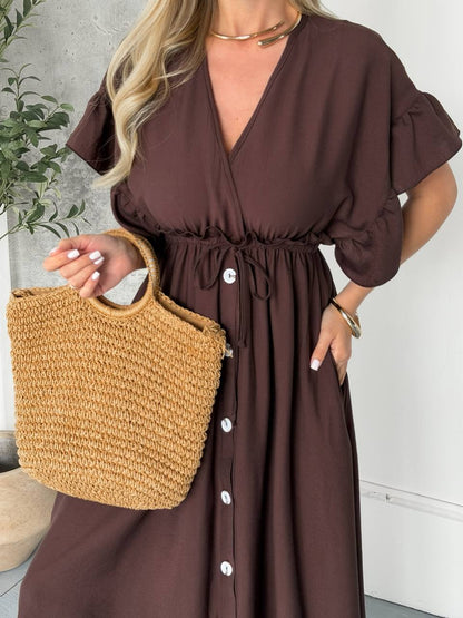 Woman wearing a brown dress holding a straw bag indoors.