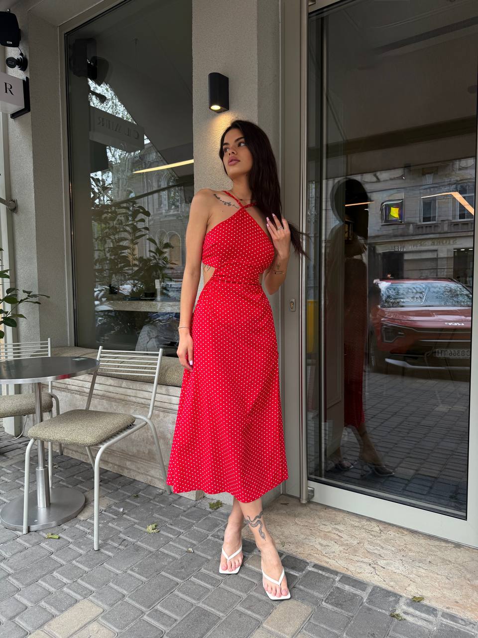 Woman in a red dress standing outside a building with a reflective surface.
