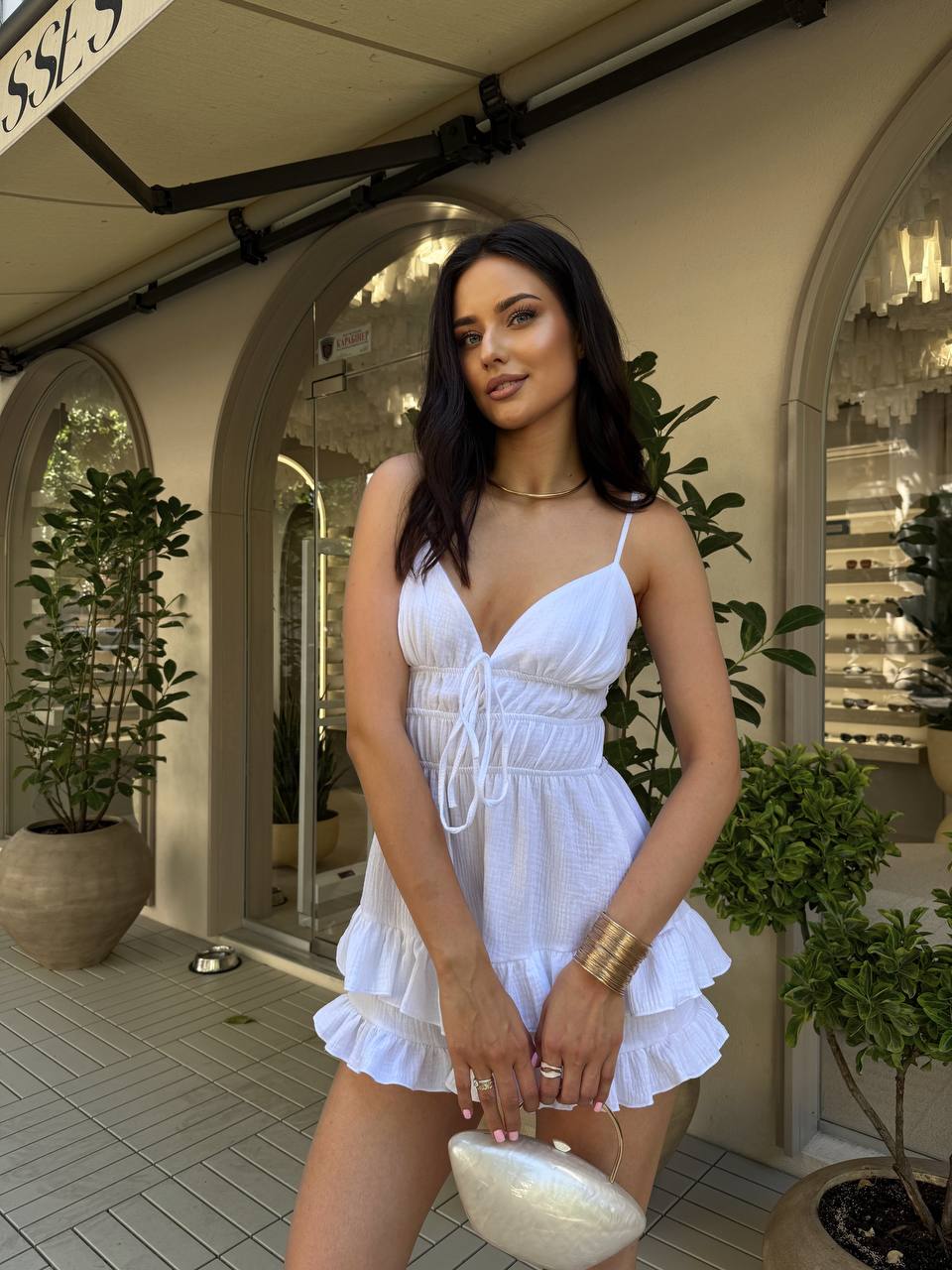 Woman in a white dress standing in an outdoor setting with plants and architectural elements.