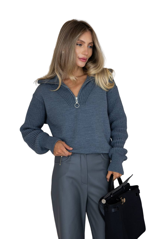 Woman wearing a blue sweater and pants holding a black handbag on a white background