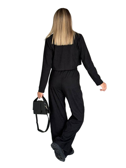 Person wearing a black outfit holding a black bag on a white background