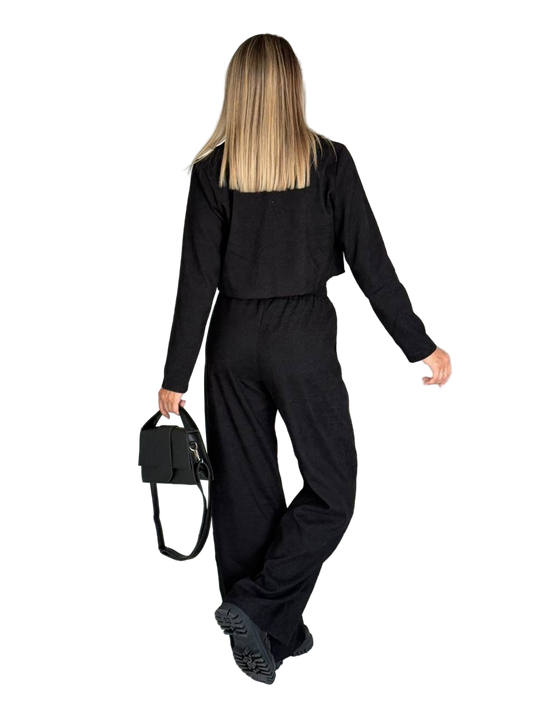 Person wearing a black outfit holding a black bag on a white background