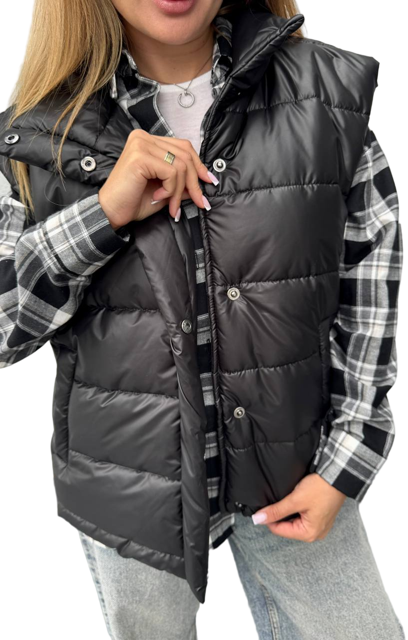 Person wearing a black puffer vest over a plaid shirt with a white background
