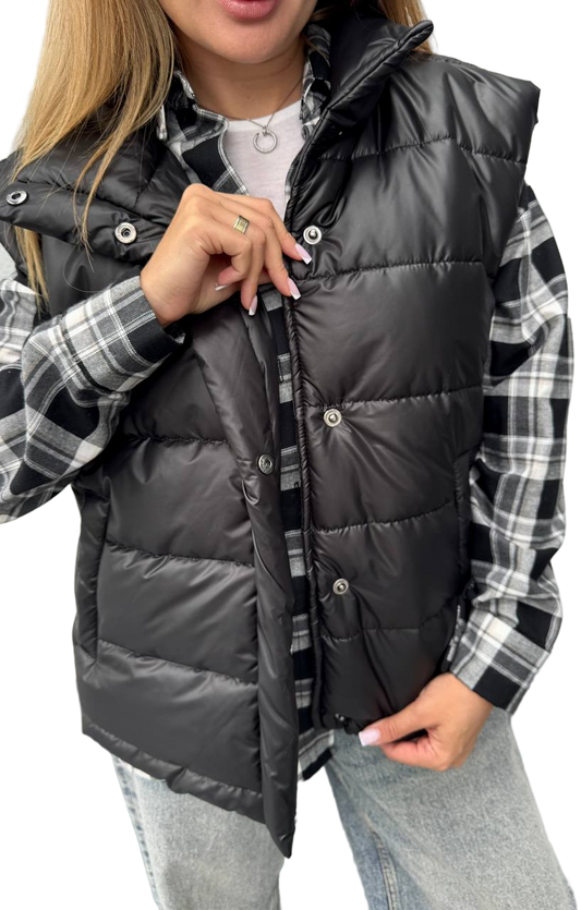 Person wearing a black puffer vest over a plaid shirt with a white background
