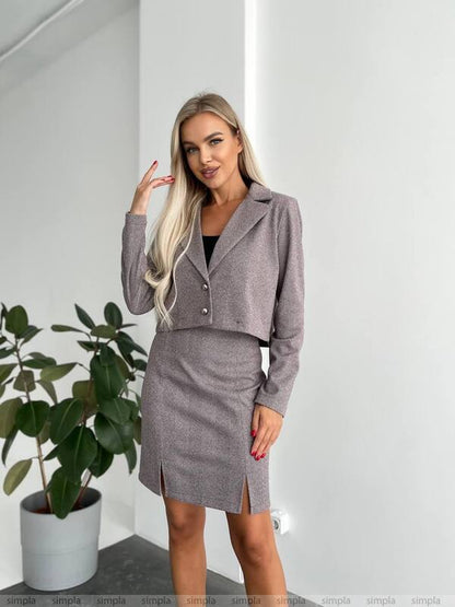 Woman wearing a gray suit with a plant in the background