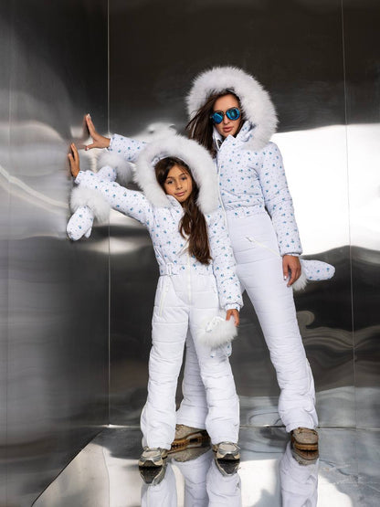 Two people in matching white puffer jackets with fur hoods on a reflective surface.