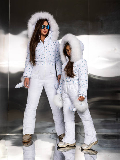 Two people in matching white winter outfits with fluffy hoods on a reflective surface.