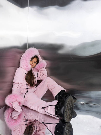 Person wearing a pink snowsuit with a hood sitting on a reflective surface.