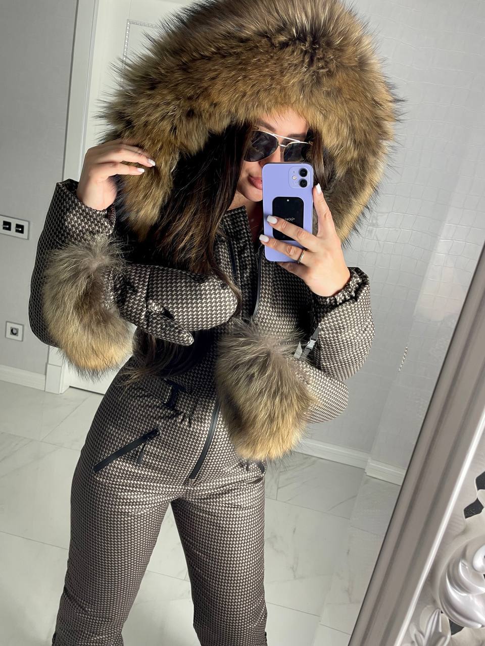 Person wearing a checkered coat with a fur-lined hood taking a mirror selfie.