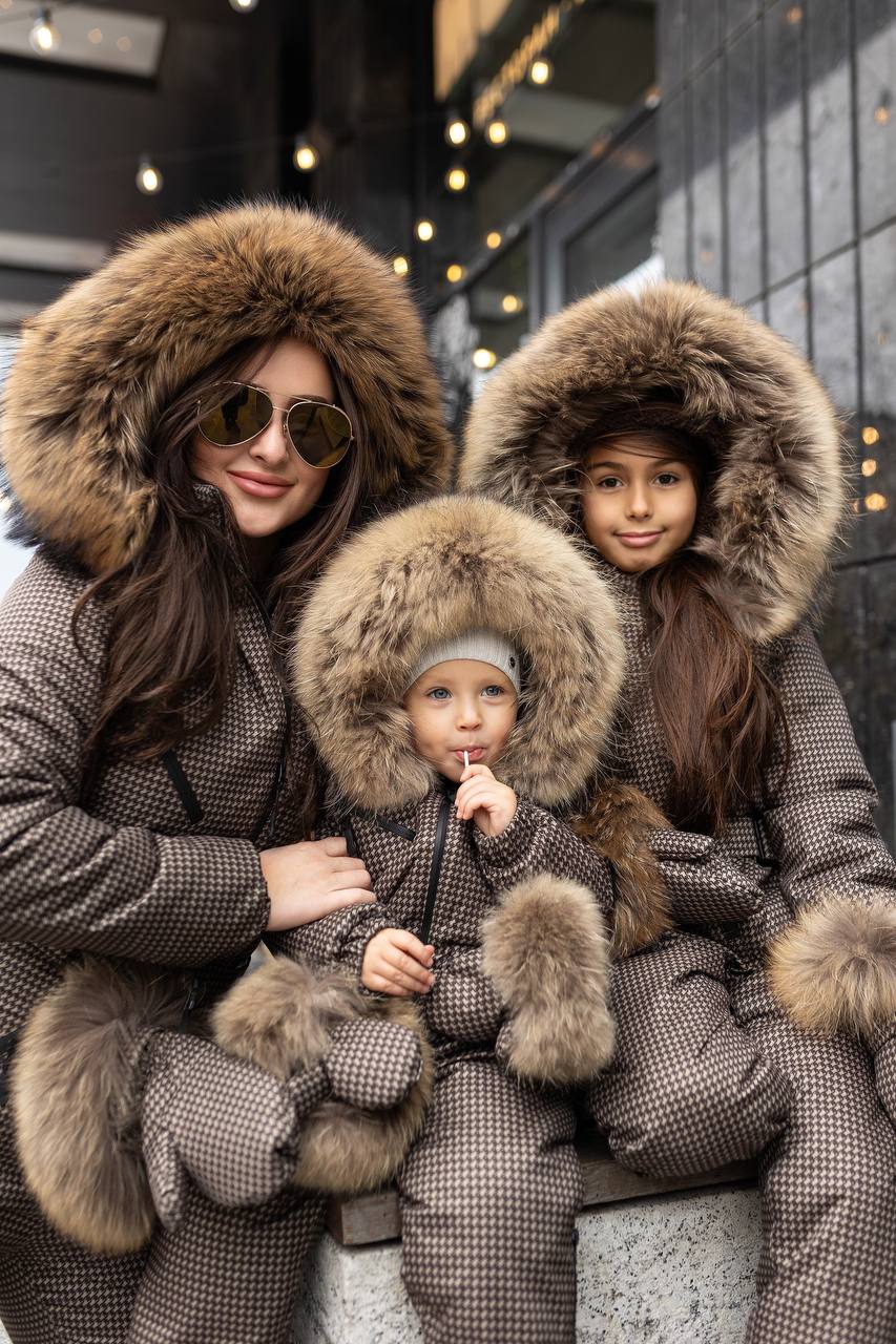 Three people wearing matching gray coats with fur hoods in an urban setting.