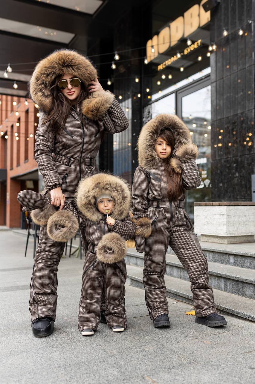 Family of three wearing matching brown winter outfits with fur hoods in front of a store.