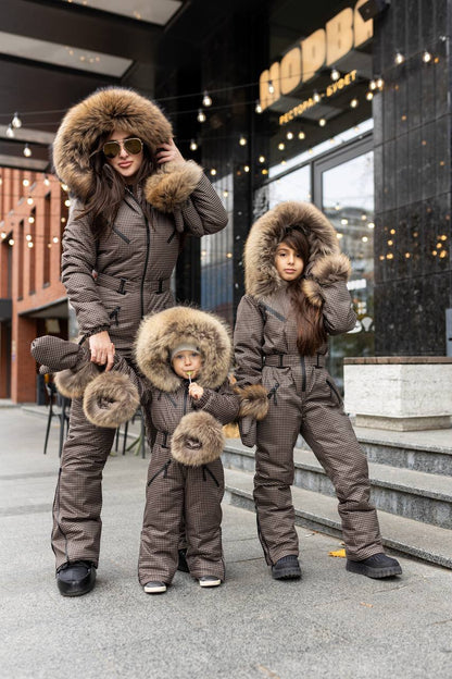 Family of three wearing matching brown winter outfits with fur hoods in front of a store.