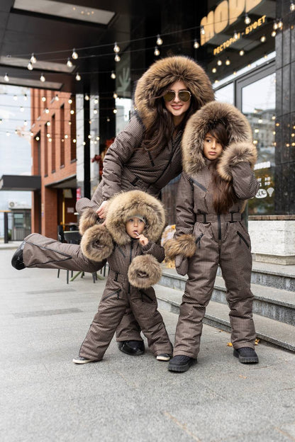 Woman and two children wearing matching brown winter outfits with fur hoods on a city street.