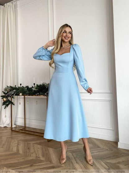 Woman wearing a light blue dress standing in a room with white walls and wooden floor.