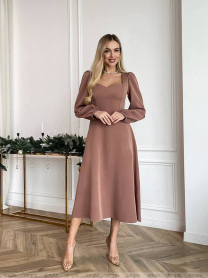Woman wearing a brown dress standing in a room with decorative elements.