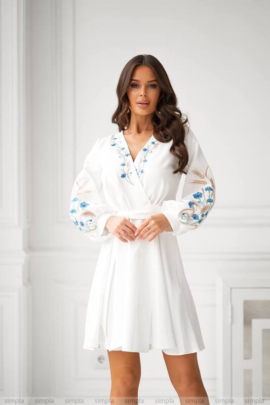 Woman wearing a white dress with floral lace sleeves against a plain background