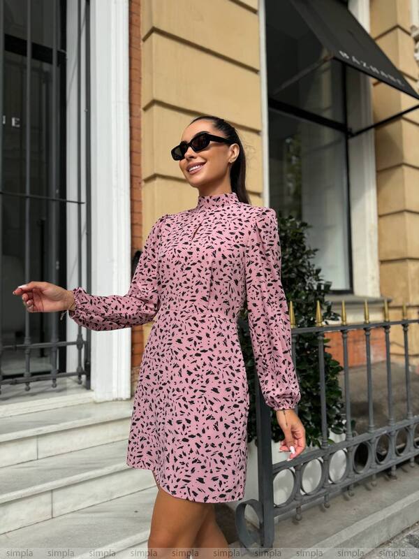 Woman wearing a pink patterned dress and sunglasses standing on a city street.