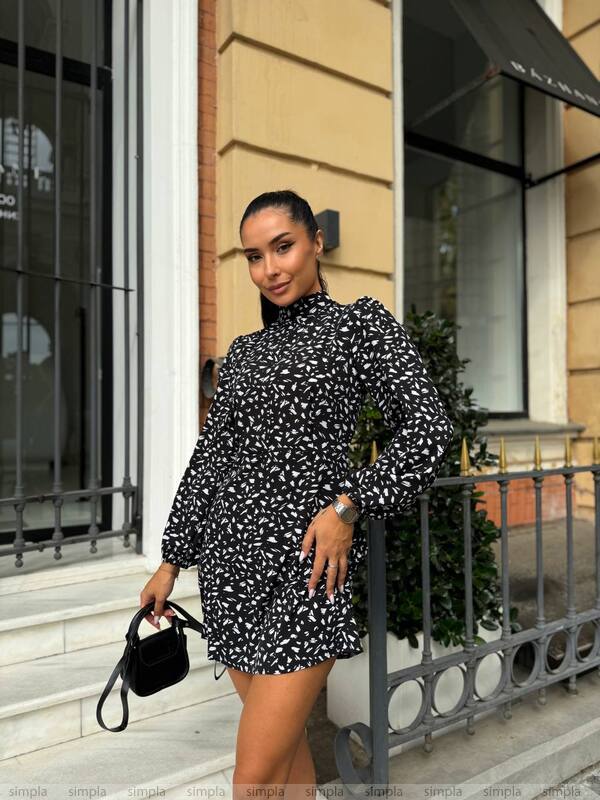 Woman in a black and white patterned dress standing outside a building.