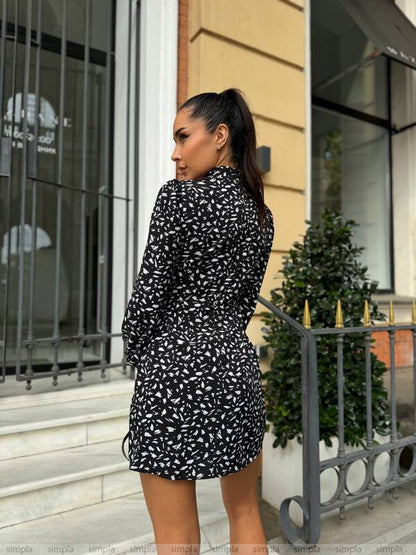 Woman in a black and white patterned dress standing outside a building.