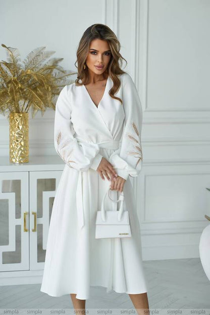 Woman wearing a white dress with gold accents in a stylish interior setting.