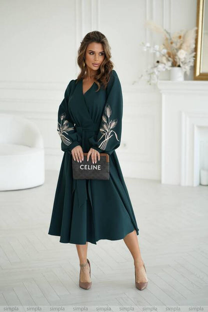 Woman wearing a dark green dress with floral embroidery, holding a Celine handbag in a white room.