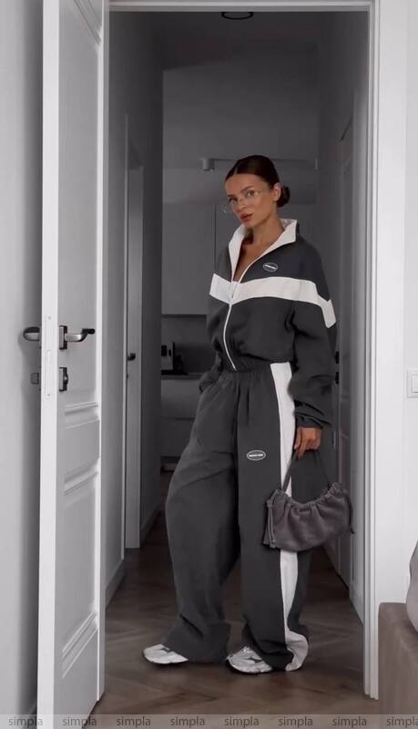 Person wearing a gray tracksuit with white accents in a room.