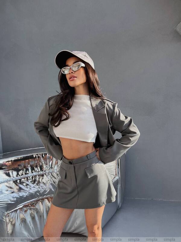 Woman in gray jacket and skirt with white top against a gray background