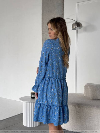 Woman wearing a blue dress with a subtle pattern in a minimalistic room.