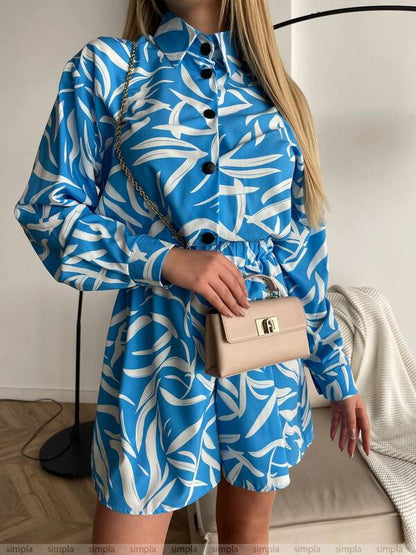 Person wearing a blue and white patterned dress holding a beige handbag indoors.
